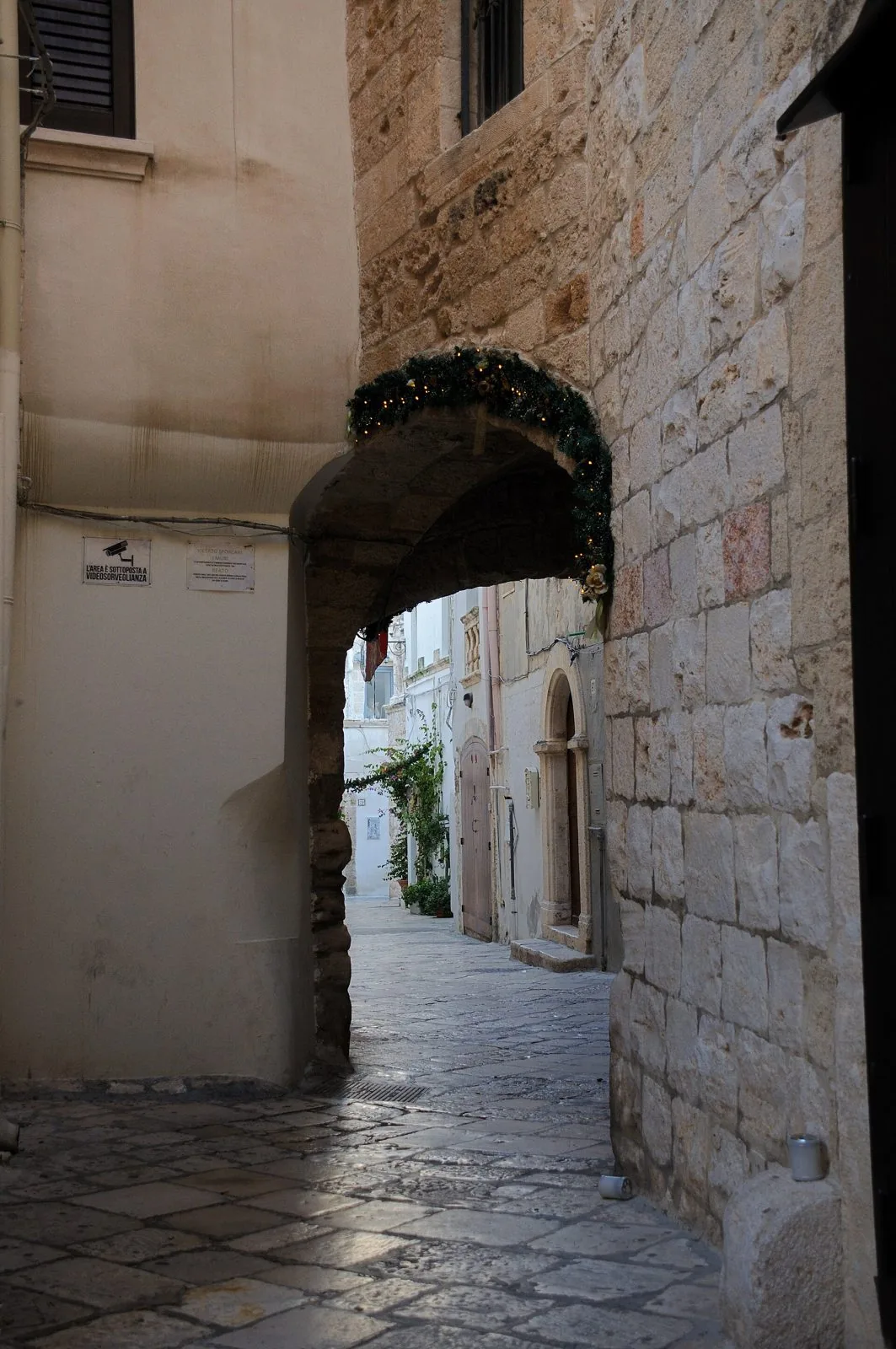 Un passaggio ad arco in pietra si apre su un vicolo lastricato del centro storico di Polignano a Mare