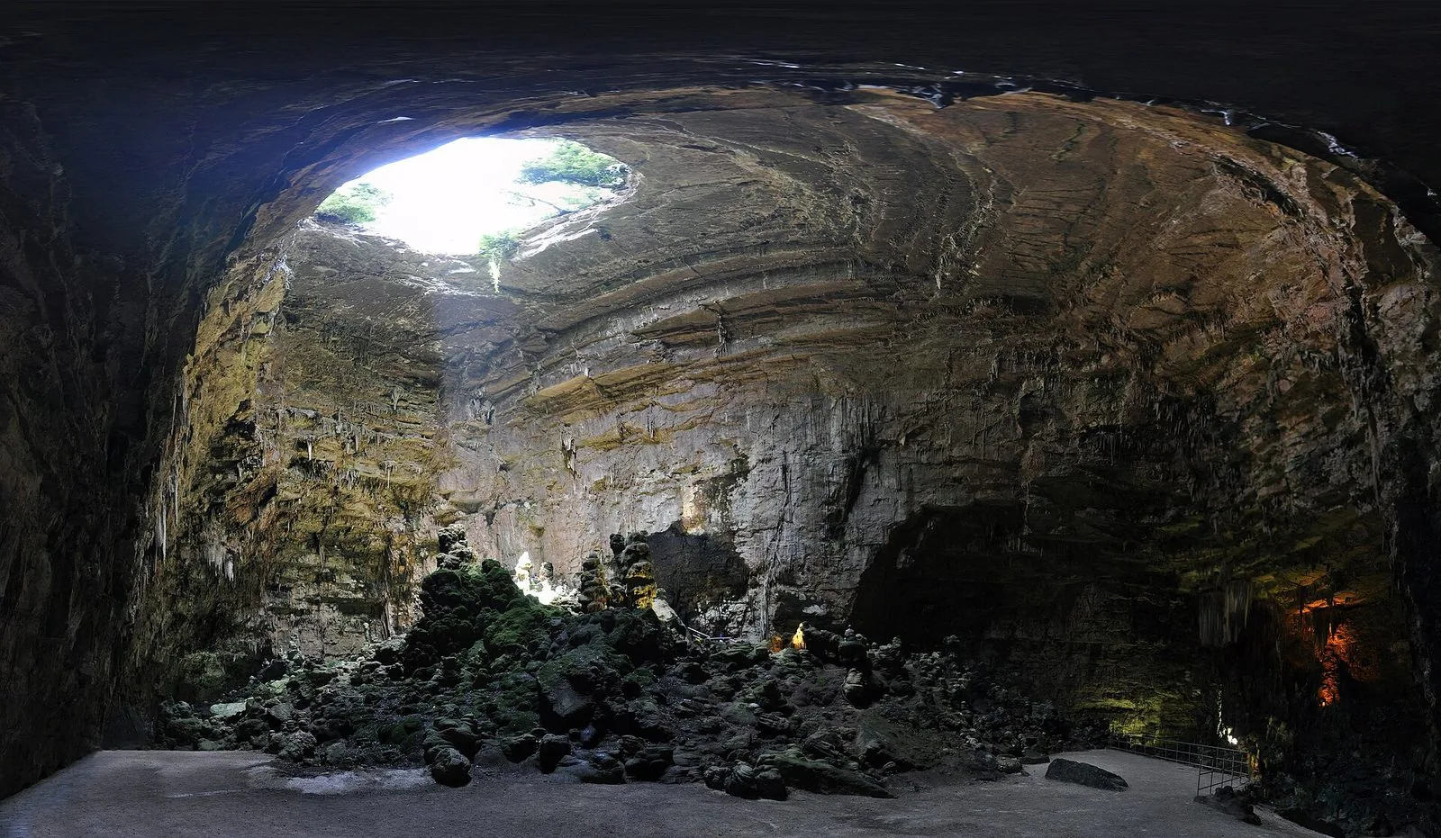La Grave delle Grotte di Castellana: vasta caverna con la volta di roccia stratificata, un'apertura da cui entra la luce del giorno e stalagmiti sul fondo
