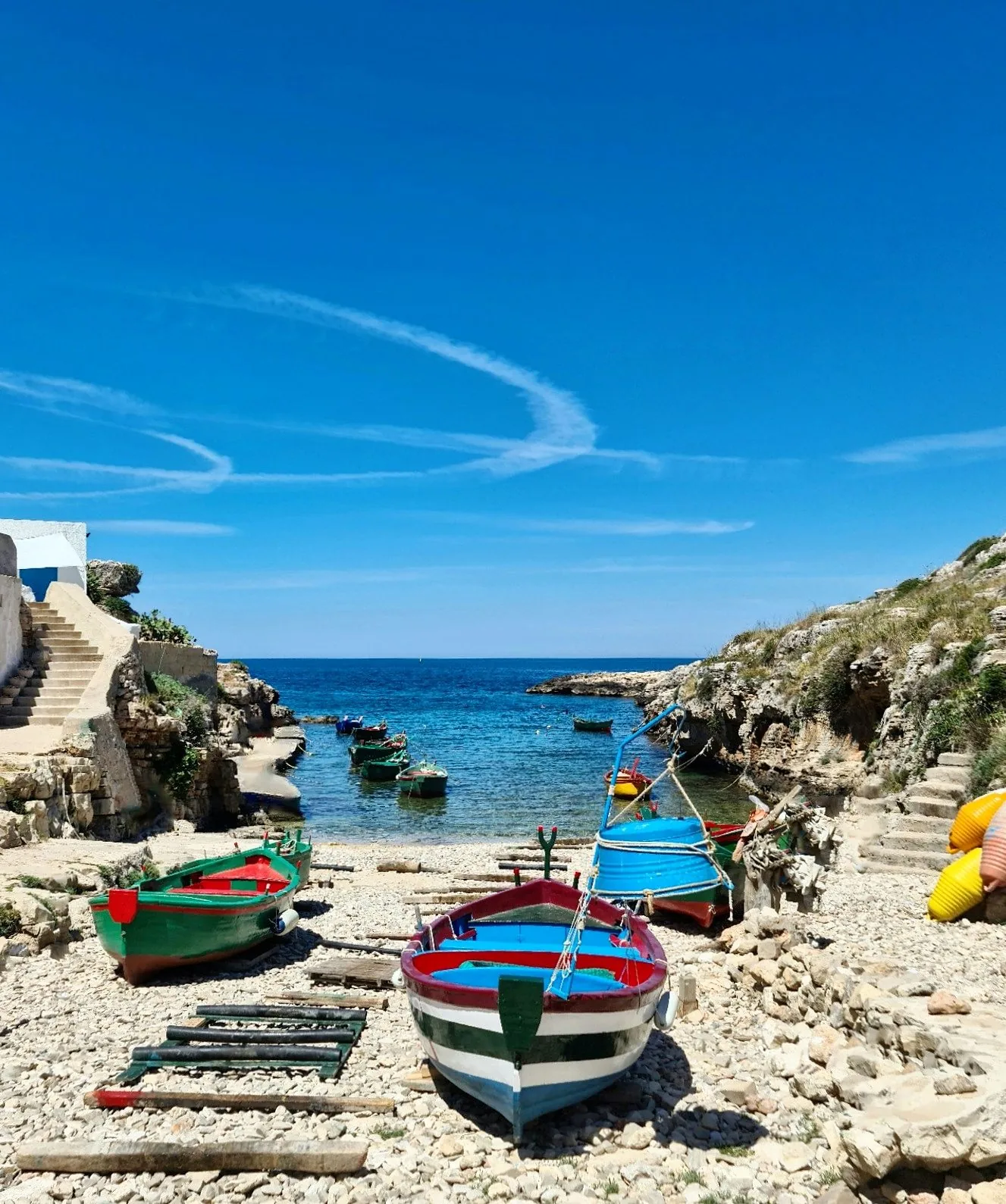 Cala Portalga a Polignano a Mare: barche di legno colorate tirate a secco sui ciottoli, il mare blu e la costa rocciosa sullo sfondo